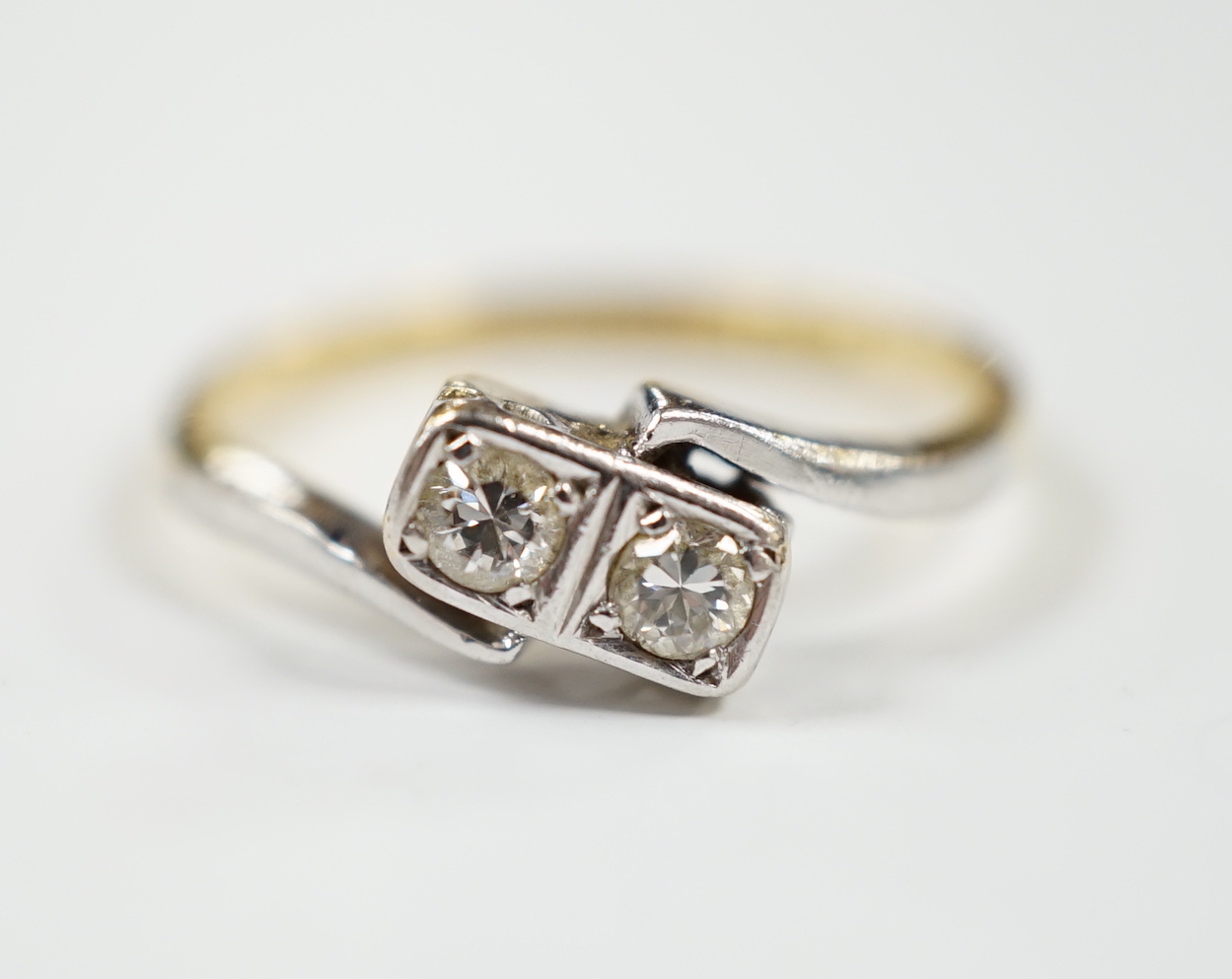 An 18ct, plat and two stone diamond set crossover ring, size M, gross weight 2.3 grams.